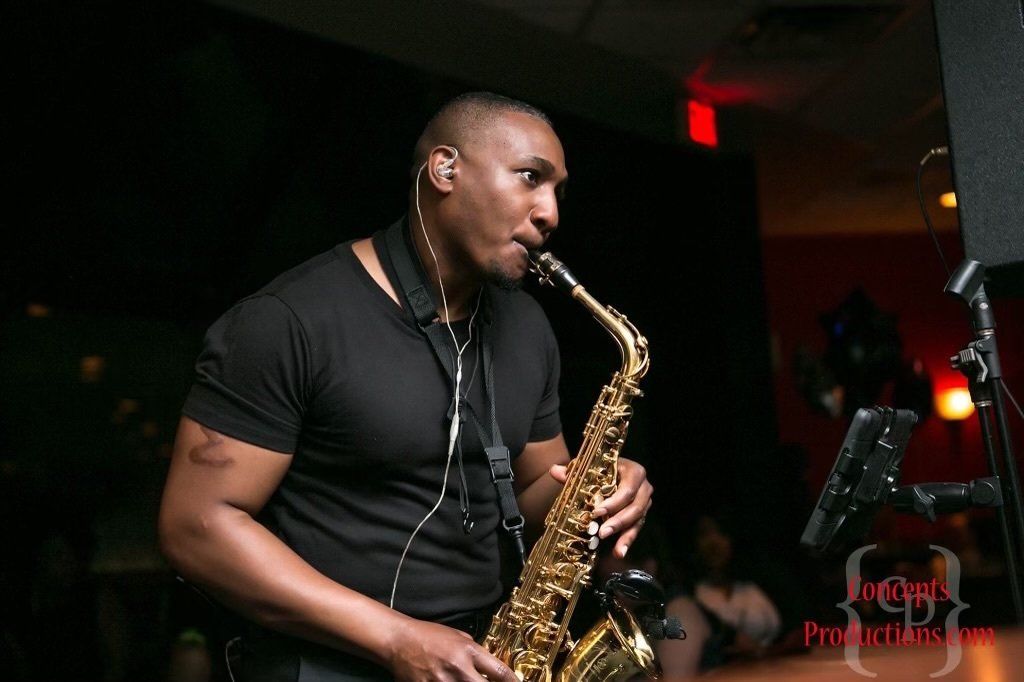 A man in a black shirt is playing a saxophone.