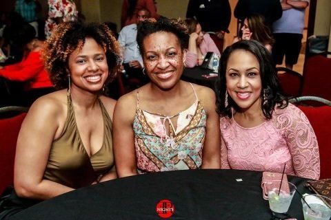 Three women are posing for a picture while sitting at a table.