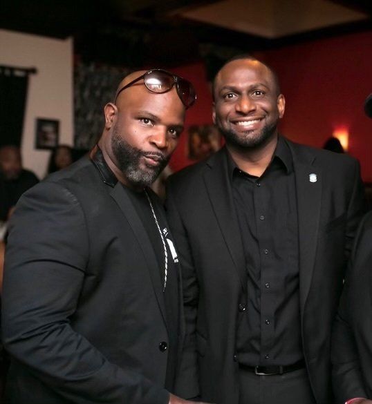 Two men are posing for a picture and one is wearing sunglasses