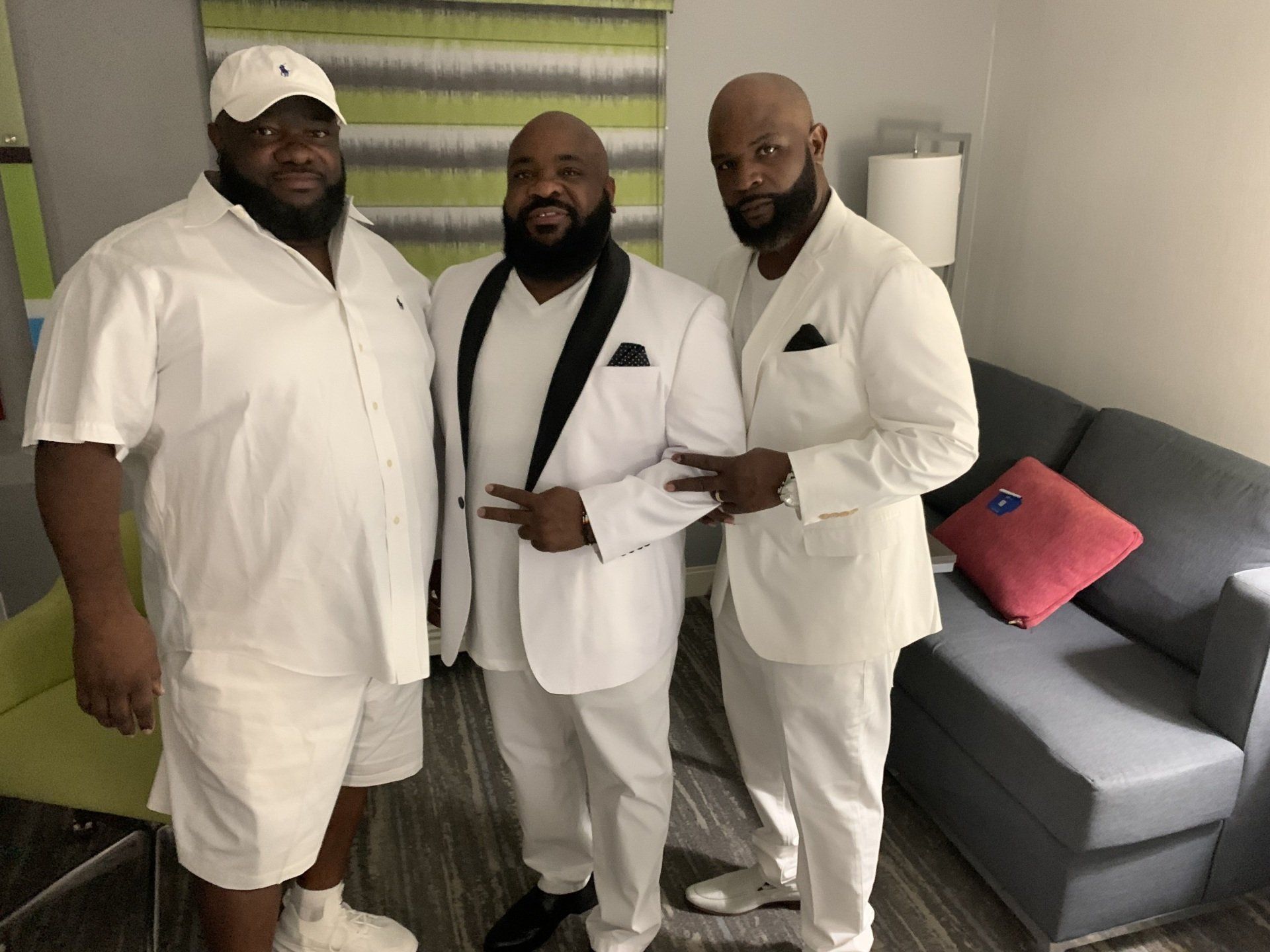 Three men in white suits are standing next to each other in a living room.