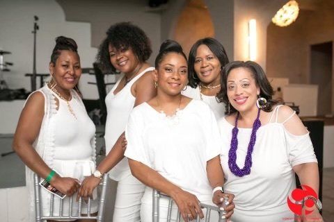 A group of women wearing white shirts and purple necklaces are posing for a picture.