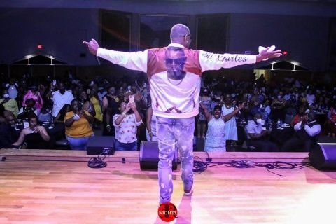 A man is standing on a stage with his arms outstretched in front of a crowd.