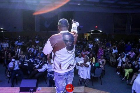 A man is standing on a stage holding a microphone in front of a crowd.