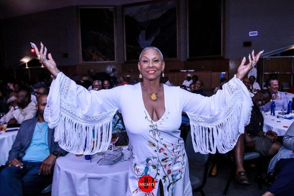 A woman in a white dress is standing in front of a table with her arms outstretched.