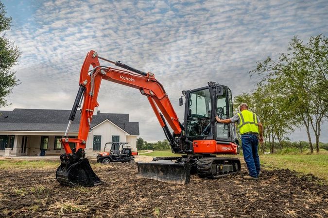 A man is standing next to an excavator in a field.