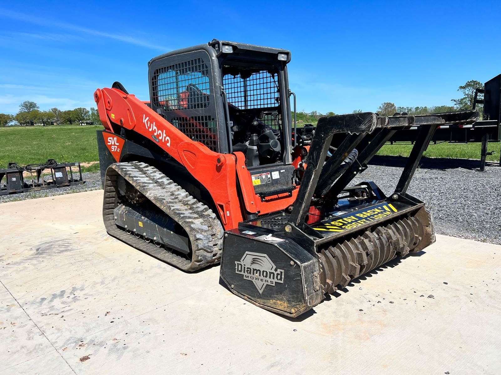 A red and black skid steer is parked in a gravel lot.