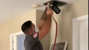 A man wearing a mask is working on a ceiling fan.