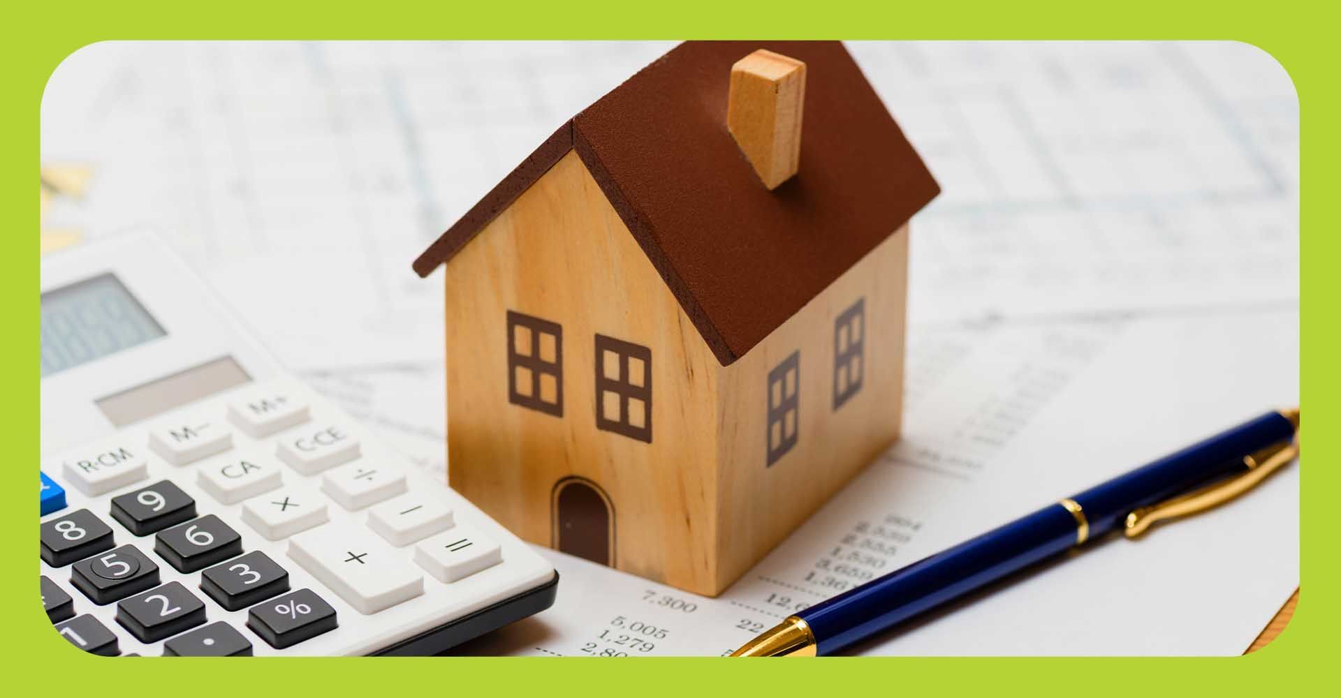Wooden house sitting on tax paperwork with a calculator