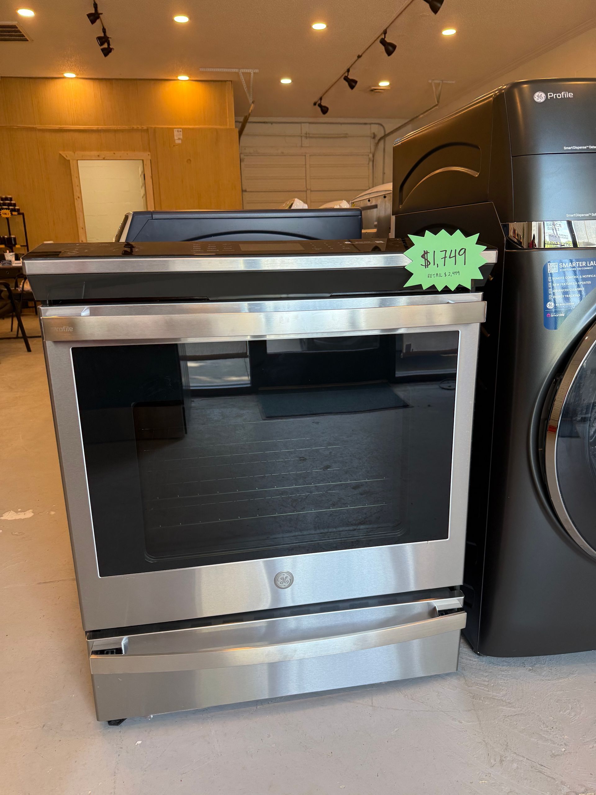 A stainless steel oven is sitting next to a black washer and dryer.