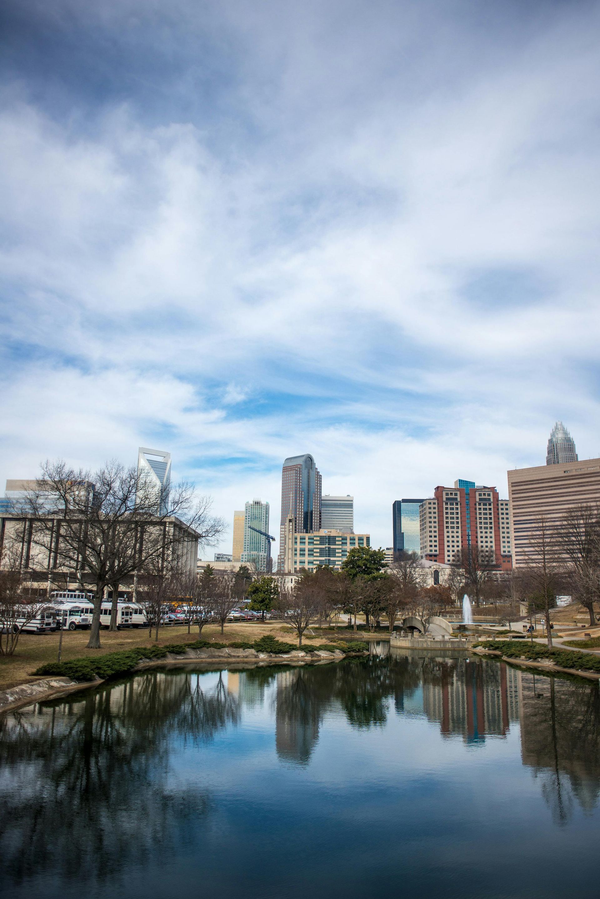 Downtown skyline reflected in calm water under a cloudy sky.