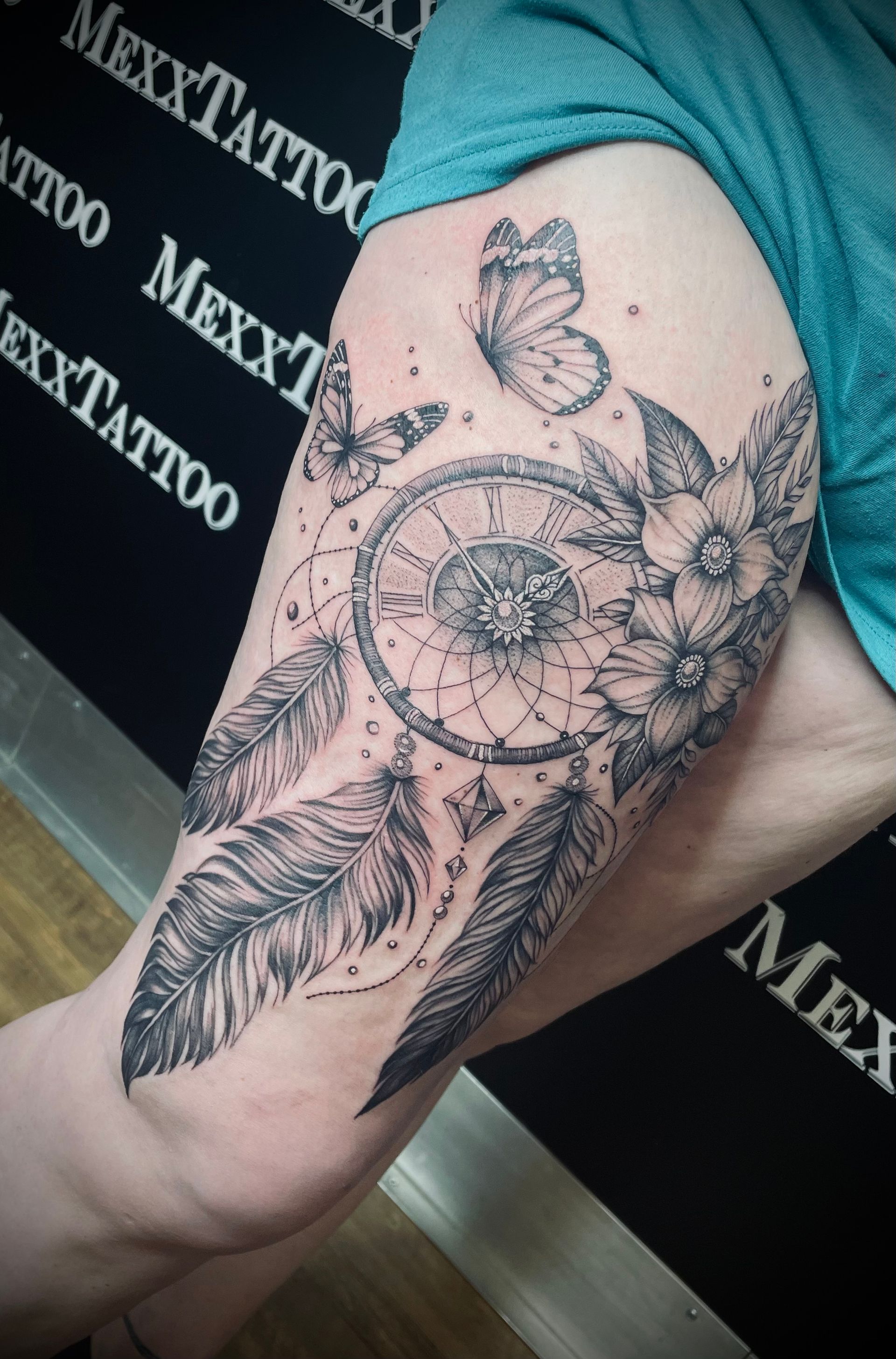 ein Schwarz-Weiß-Tattoo eines Traumfängers mit Federn und Schmetterlingen