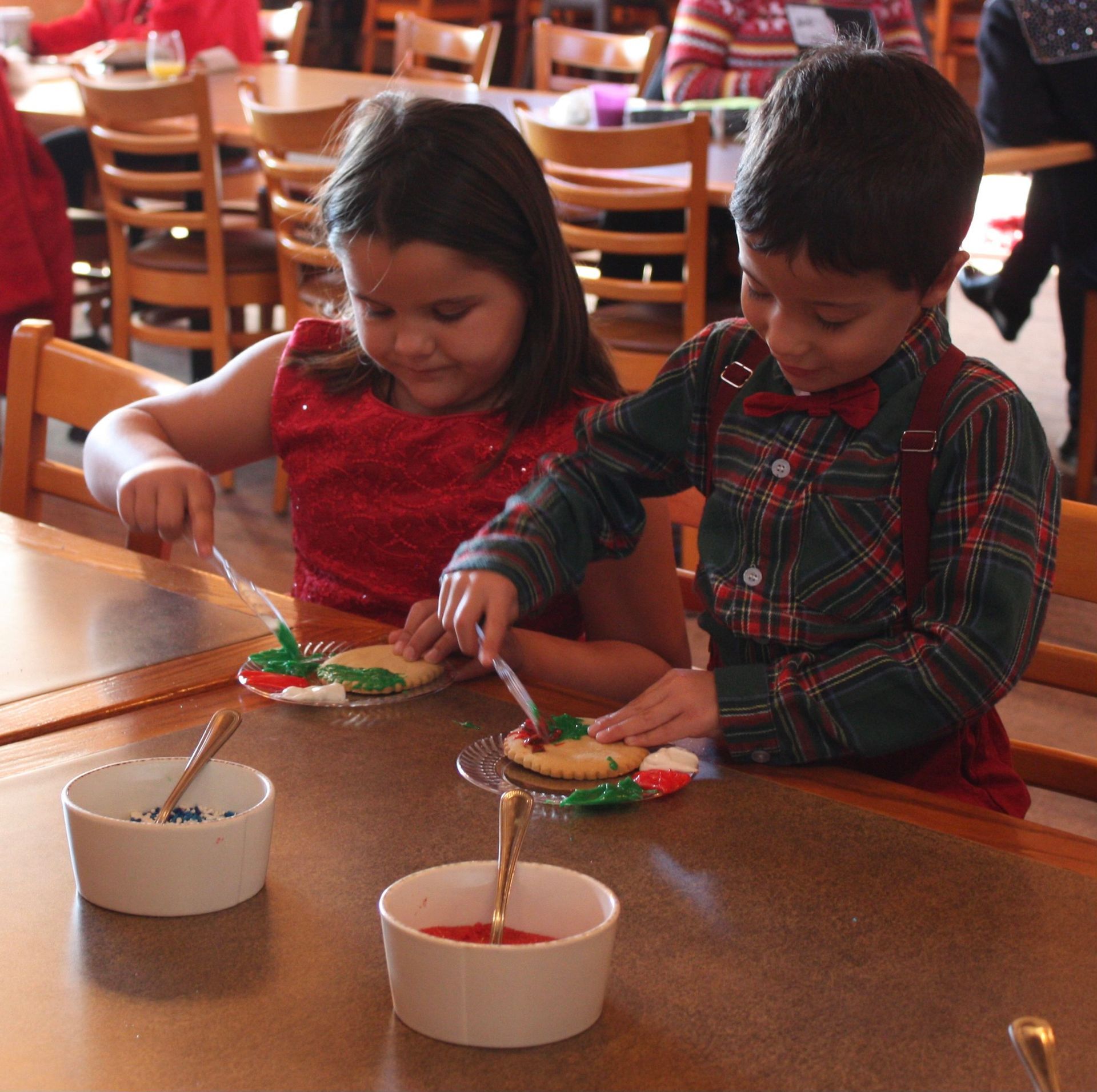 Two children decorating cookies at a table. Bowls of frosting and decorating tools are present.