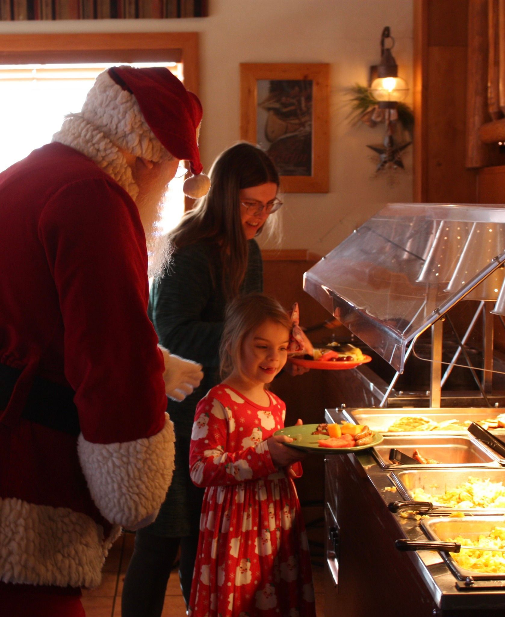 Santa at a buffet with a woman and child, the child holding a plate of food.