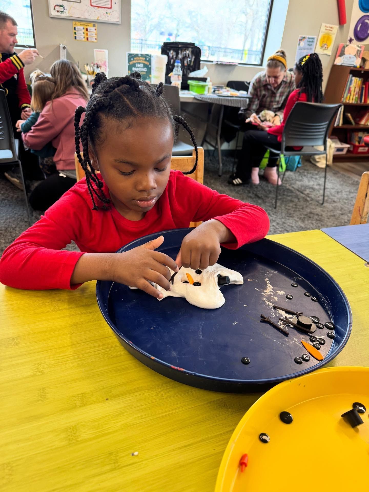 Young child focused on creating a craft with clay and decorations at a table.