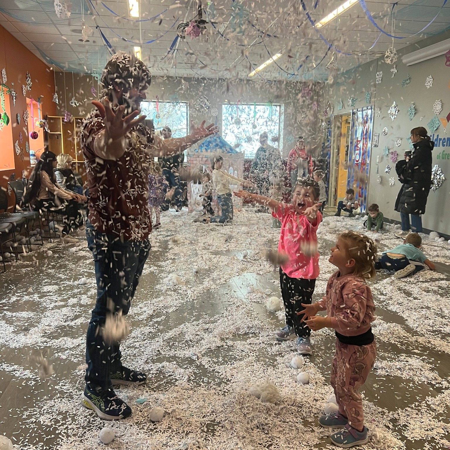 People playing in a room with falling artificial snow. Man and children are reaching up with joy.