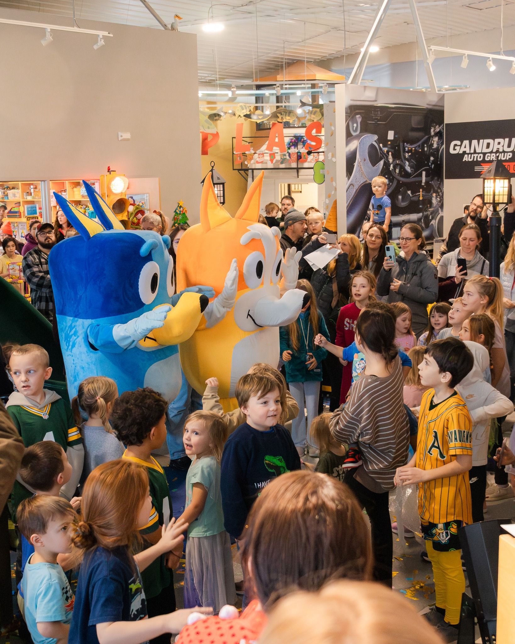 Two costumed characters surrounded by children in a brightly lit store.