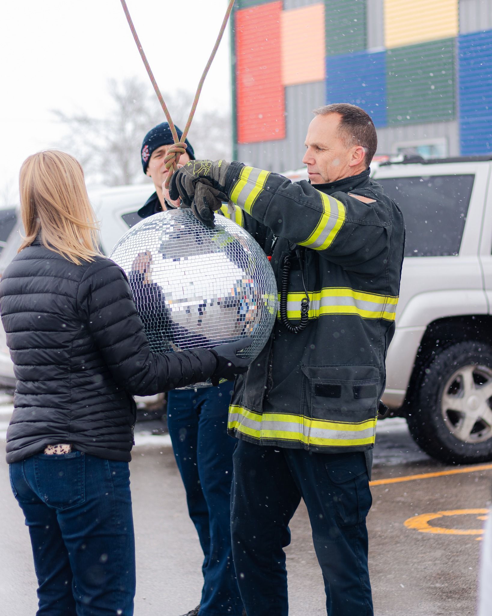 Three people holding a large disco ball outdoors, one in firefighter gear.