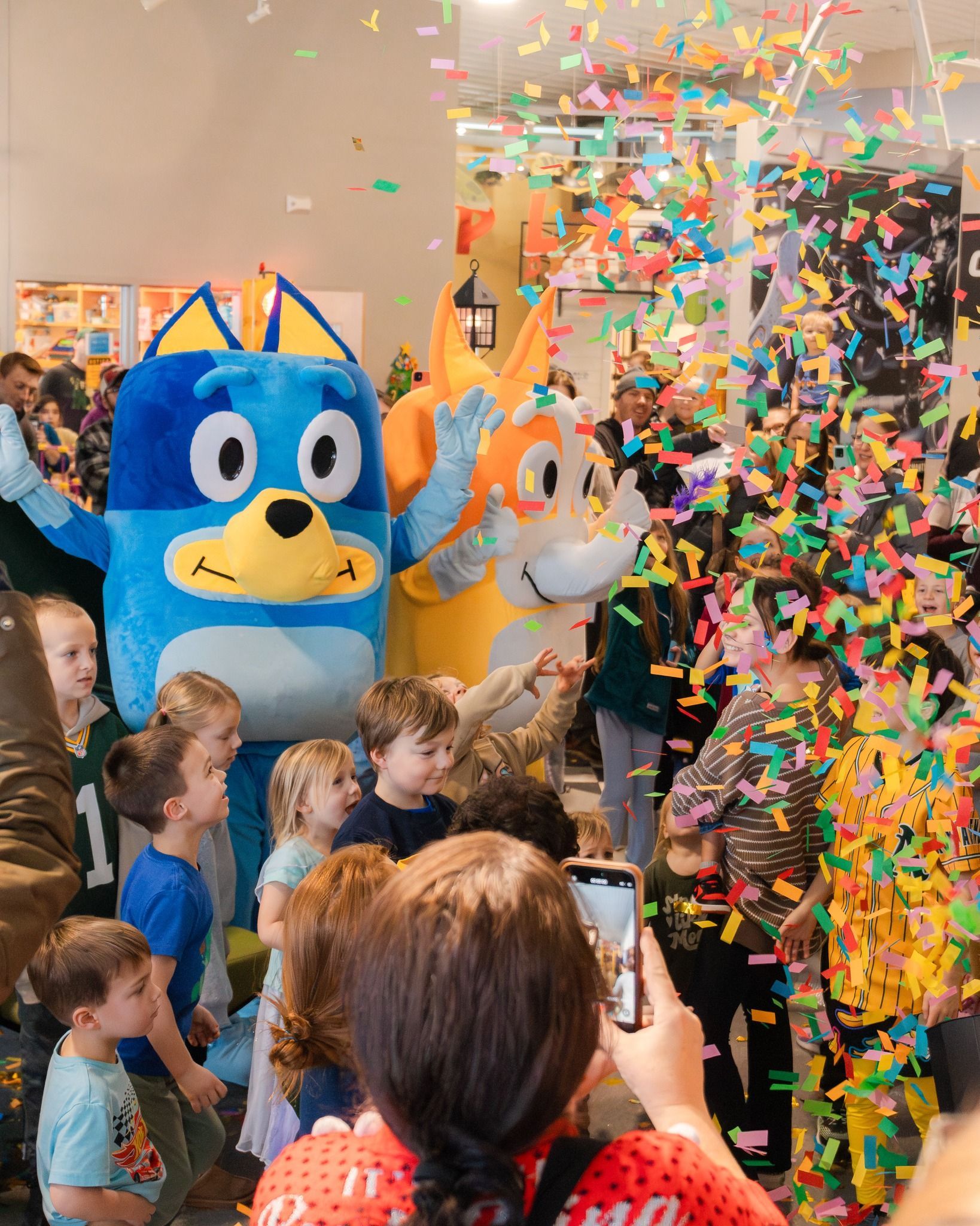 Santa sits in a red sleigh with elves outdoors; a reindeer stands nearby. Everyone smiles.