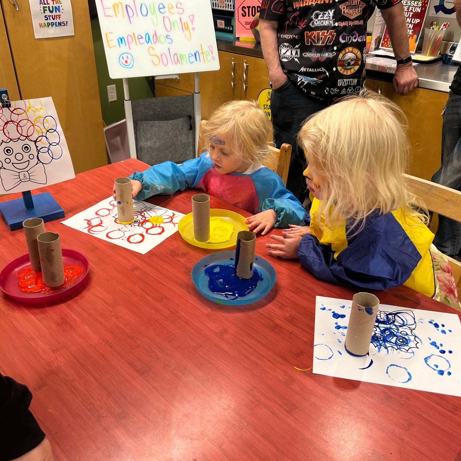 Two young children painting with toilet paper rolls and paint at a table.