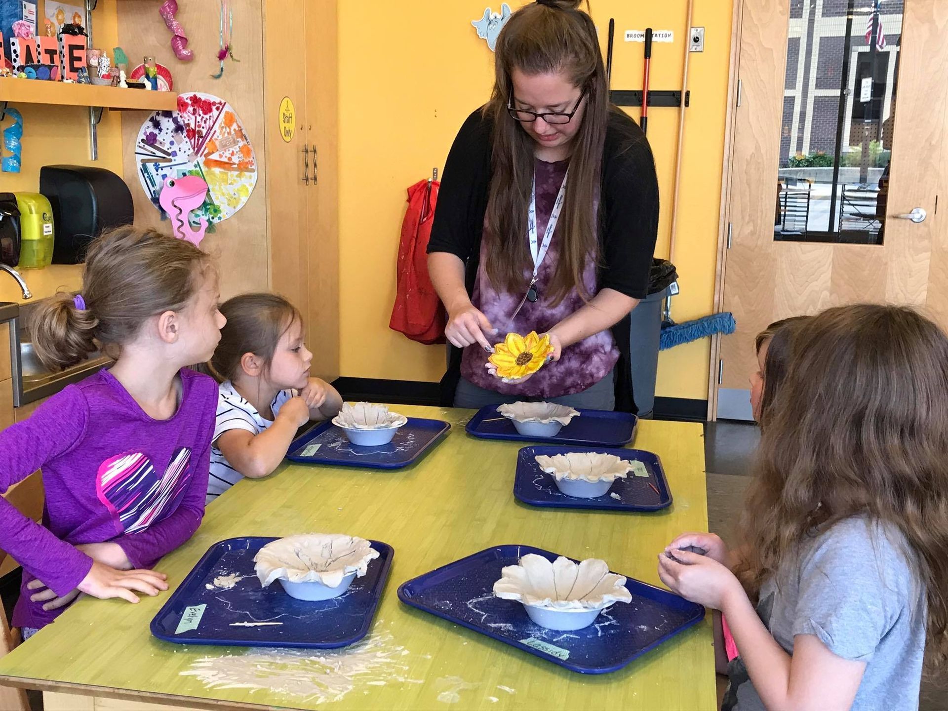 A woman is teaching a group of young girls how to make clay flowers.