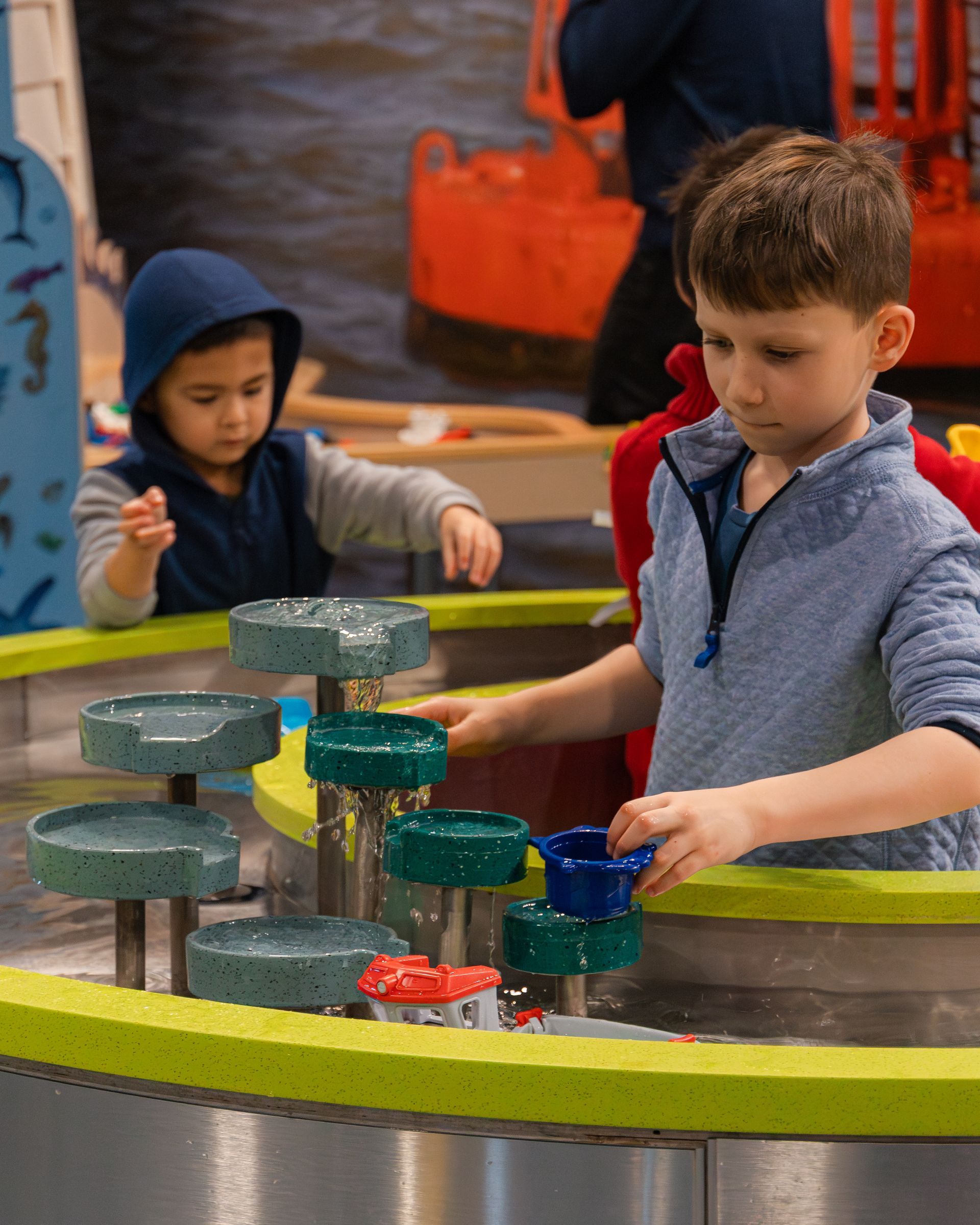Two children playing with a water feature. One pours water, the other watches.