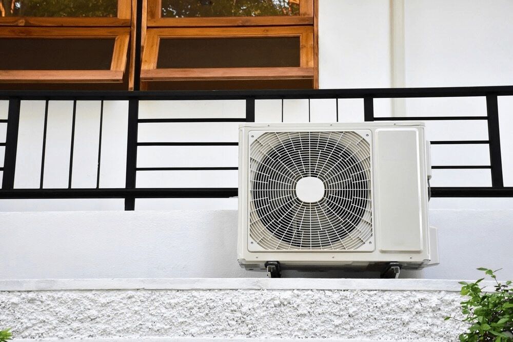 A White Air Conditioner is Sitting on the Side of a Building Next to a Window — First Point Air Conditioning in Fyshwick, ACT