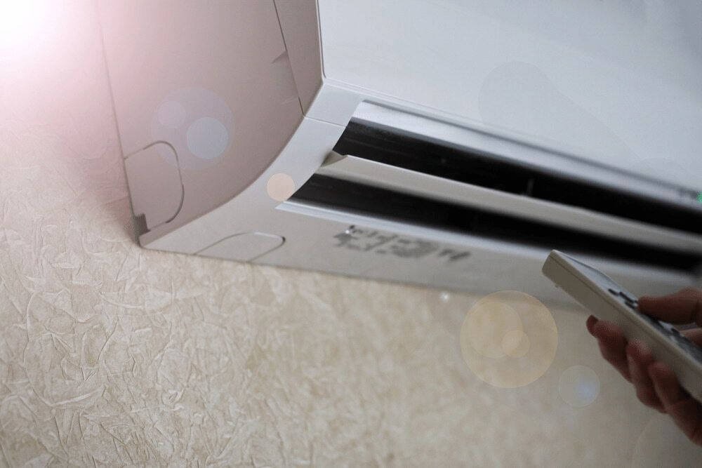 a Person is Using a Remote Control to Turn on an Air Conditioner — First Point Air Conditioning in Fyshwick, ACT