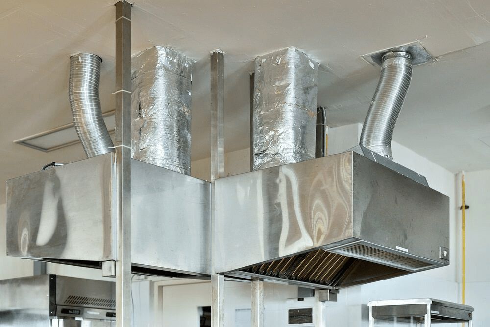 A Stainless Steel Exhaust Hood is Hanging From the Ceiling of a Kitchen— First Point Air Conditioning in Fyshwick, ACT