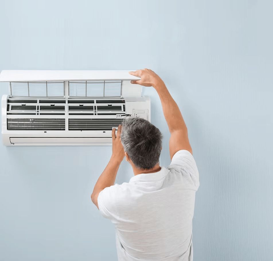 A Man is Cleaning an Air Conditioner on a Wall — First Point Air Conditioning in Fyshwick, ACT