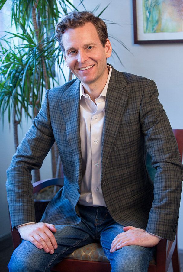 A man in a suit is sitting in a chair with his hands on his knees.