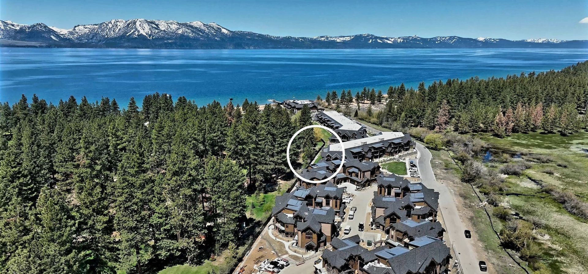 An aerial view of a house next to a lake with mountains in the background.