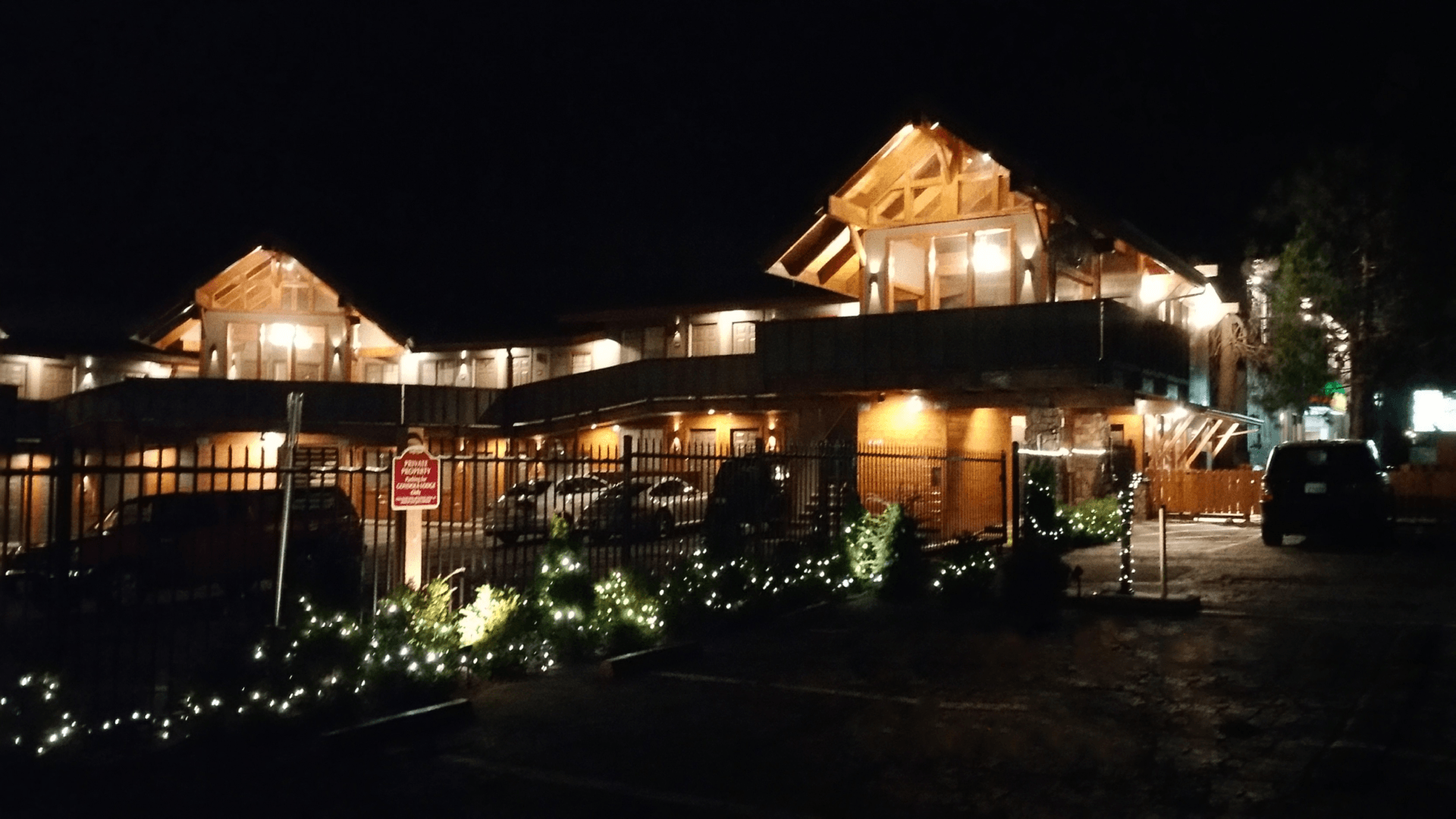A large building with security gating  is lit up at night with cars parked in front of it