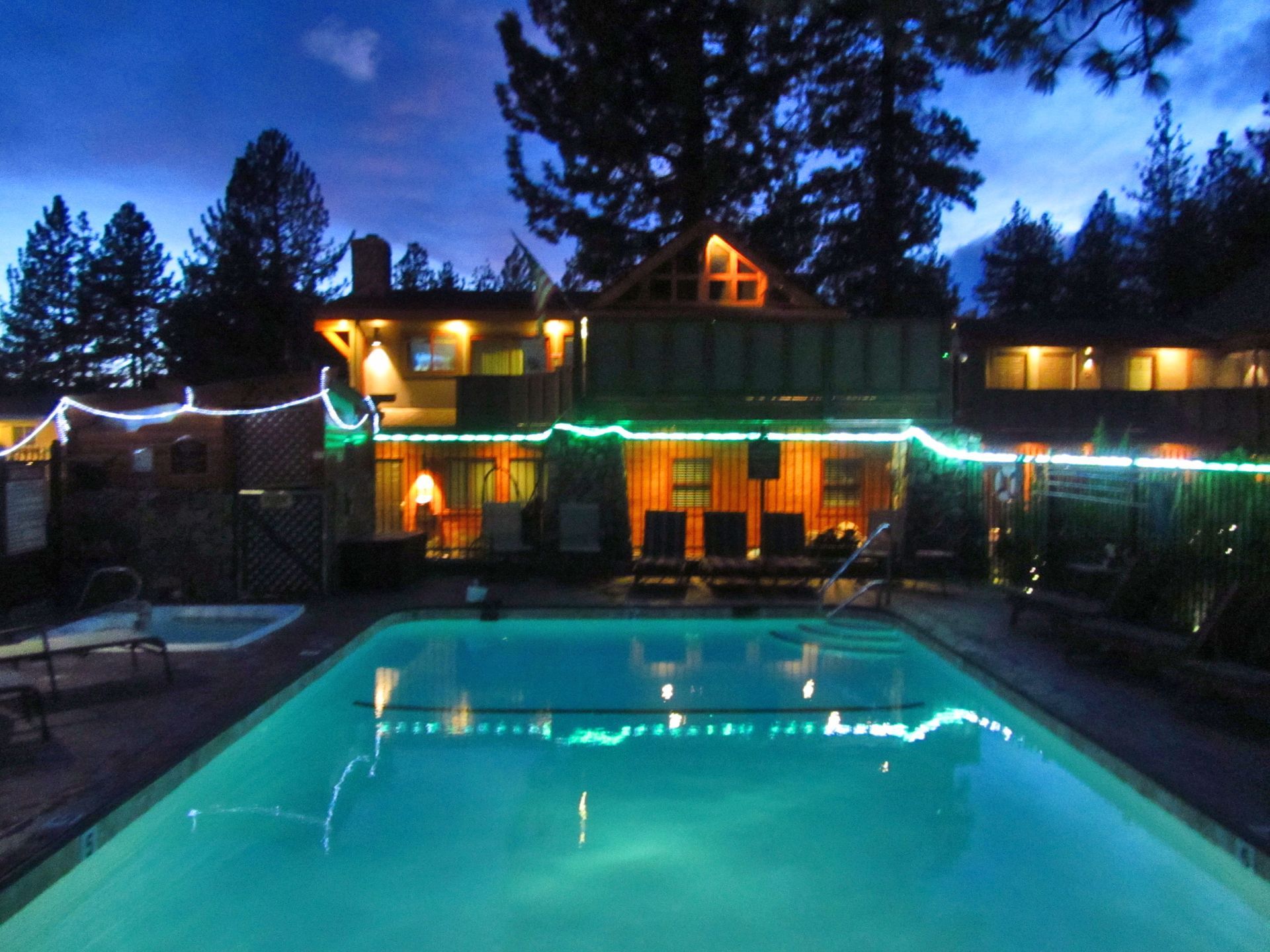 A large swimming pool is lit up at night in front of a house