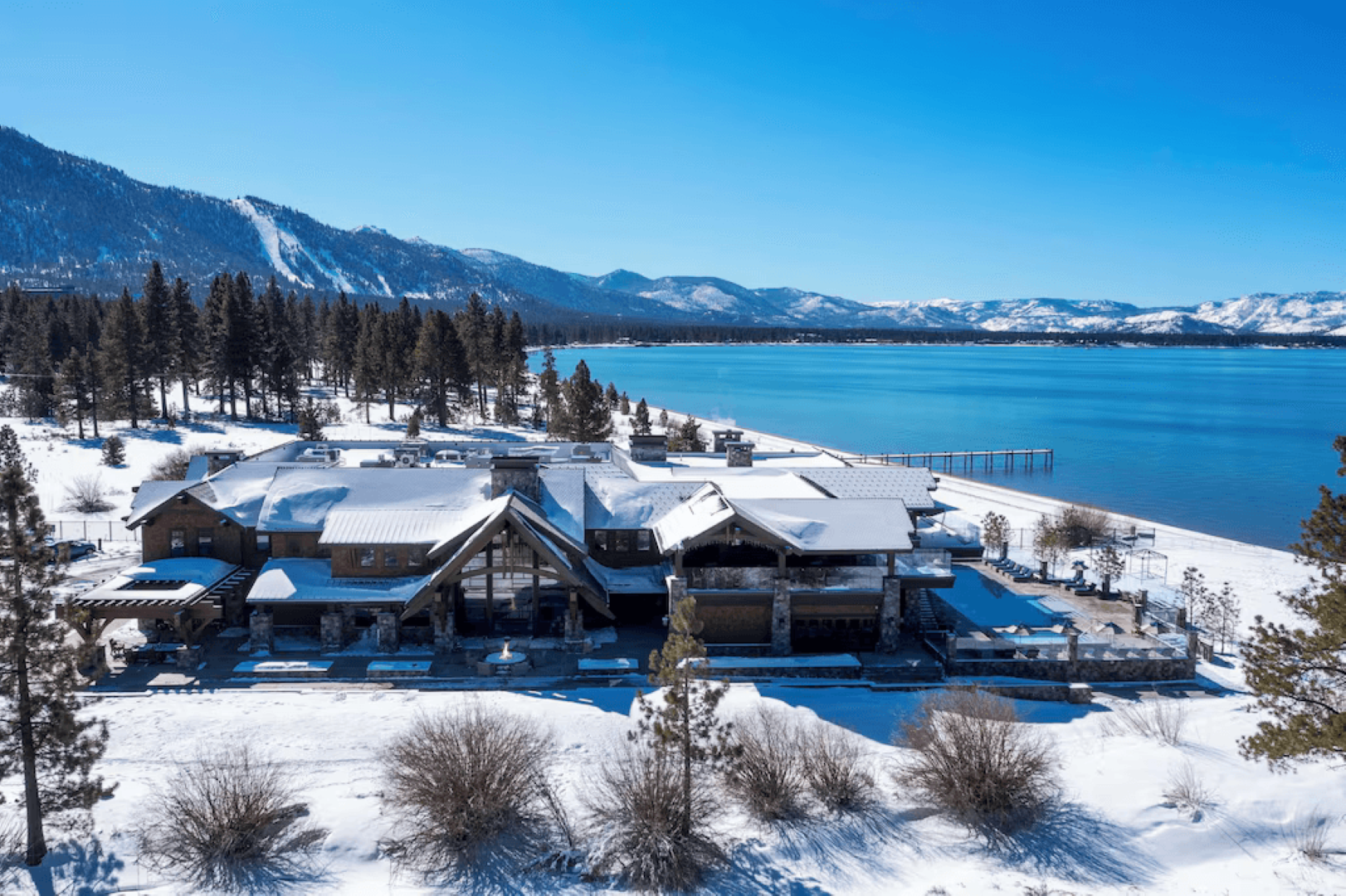 An aerial view of a large house surrounded by snow next to a lake.