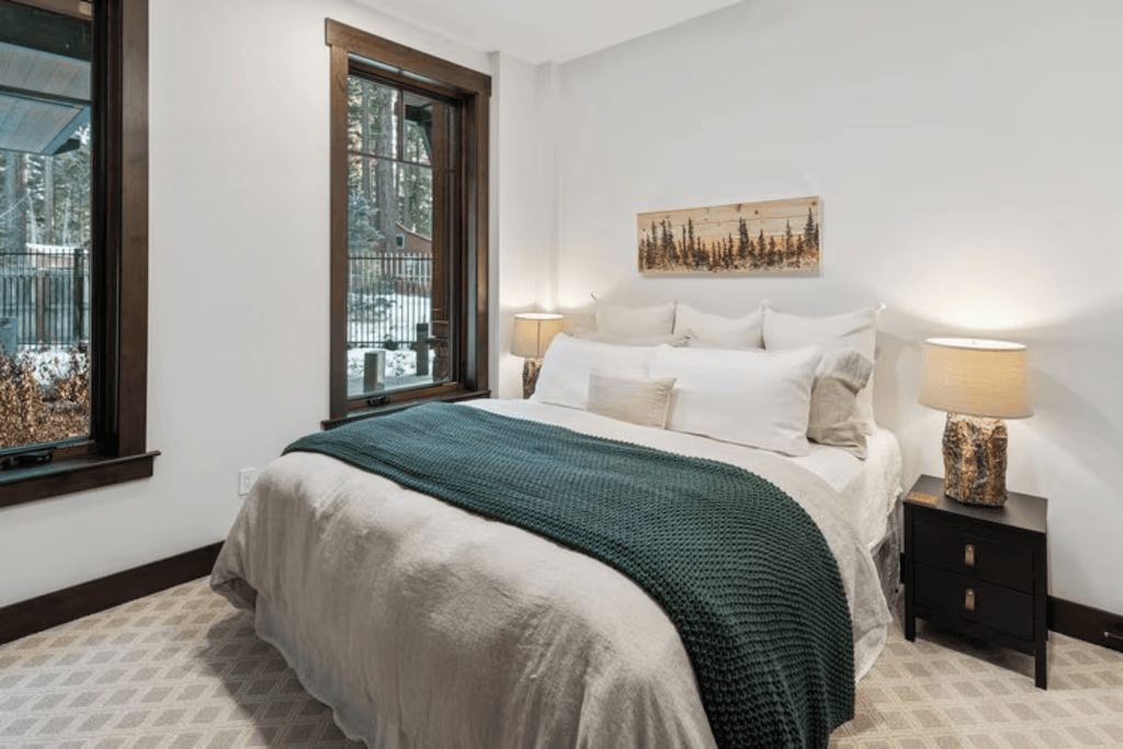A bedroom with a bed , nightstand , lamps and a window.