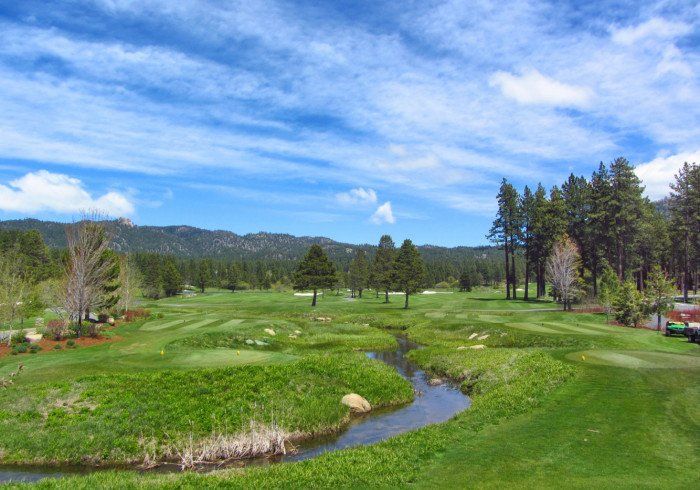 A golf course with a stream running through it and mountains in the background.