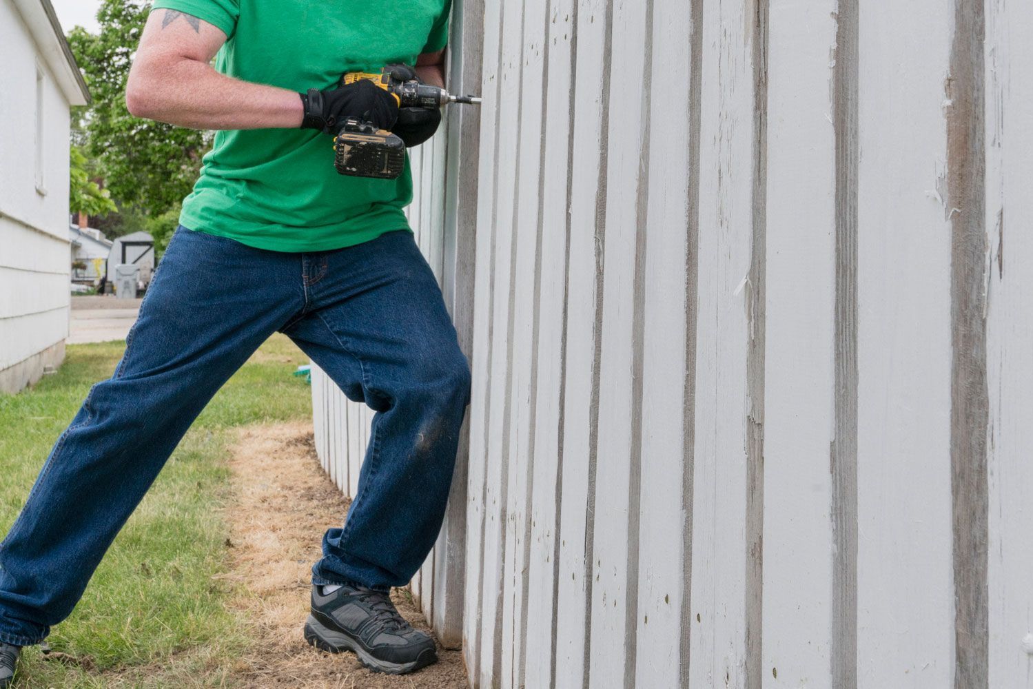 A man is using a drill to fix a fence.