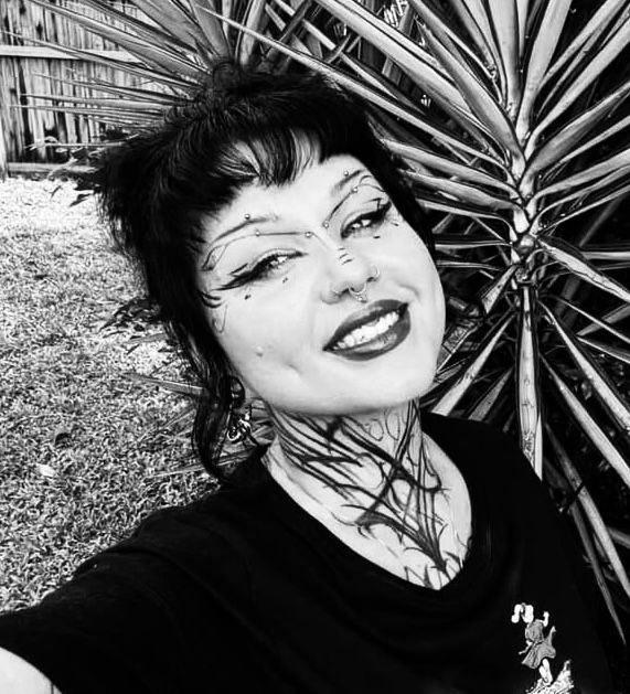 Person with intricate face and neck makeup, smiling outdoors by a palm tree — Pins and Needles Tattoo in Trinity Beach, QLD