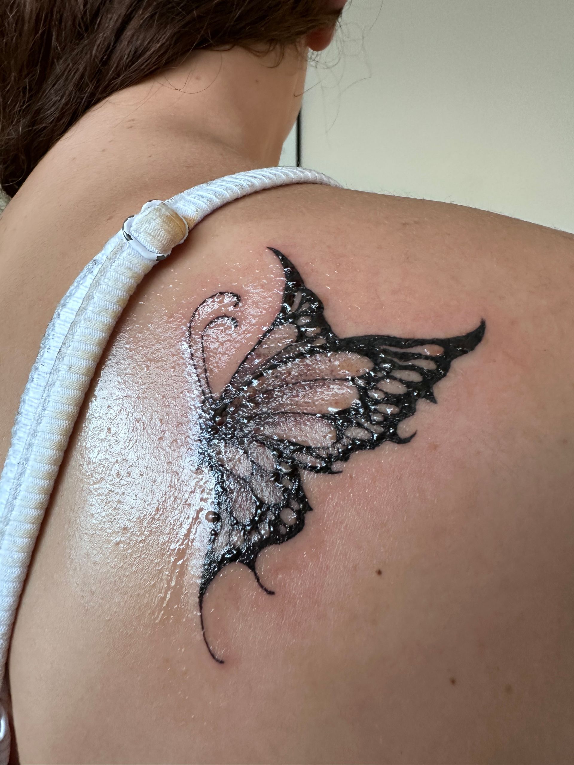 Black butterfly tattoo on shoulder, right wing detailed, left wing speckled, skin toned. — Pins and Needles Tattoo in Smithfield, QLD