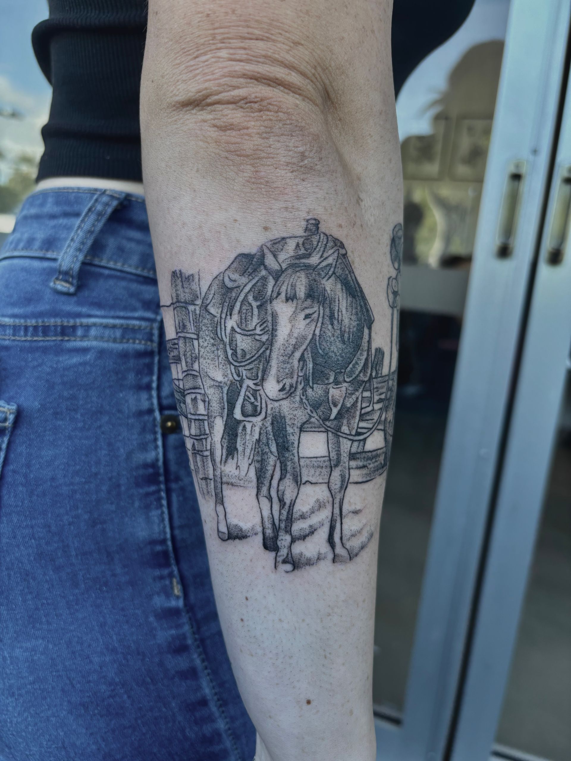 Black and white arm tattoo of a person riding a horse with buildings in the background. — Pins and Needles Tattoo in Smithfield, QLD