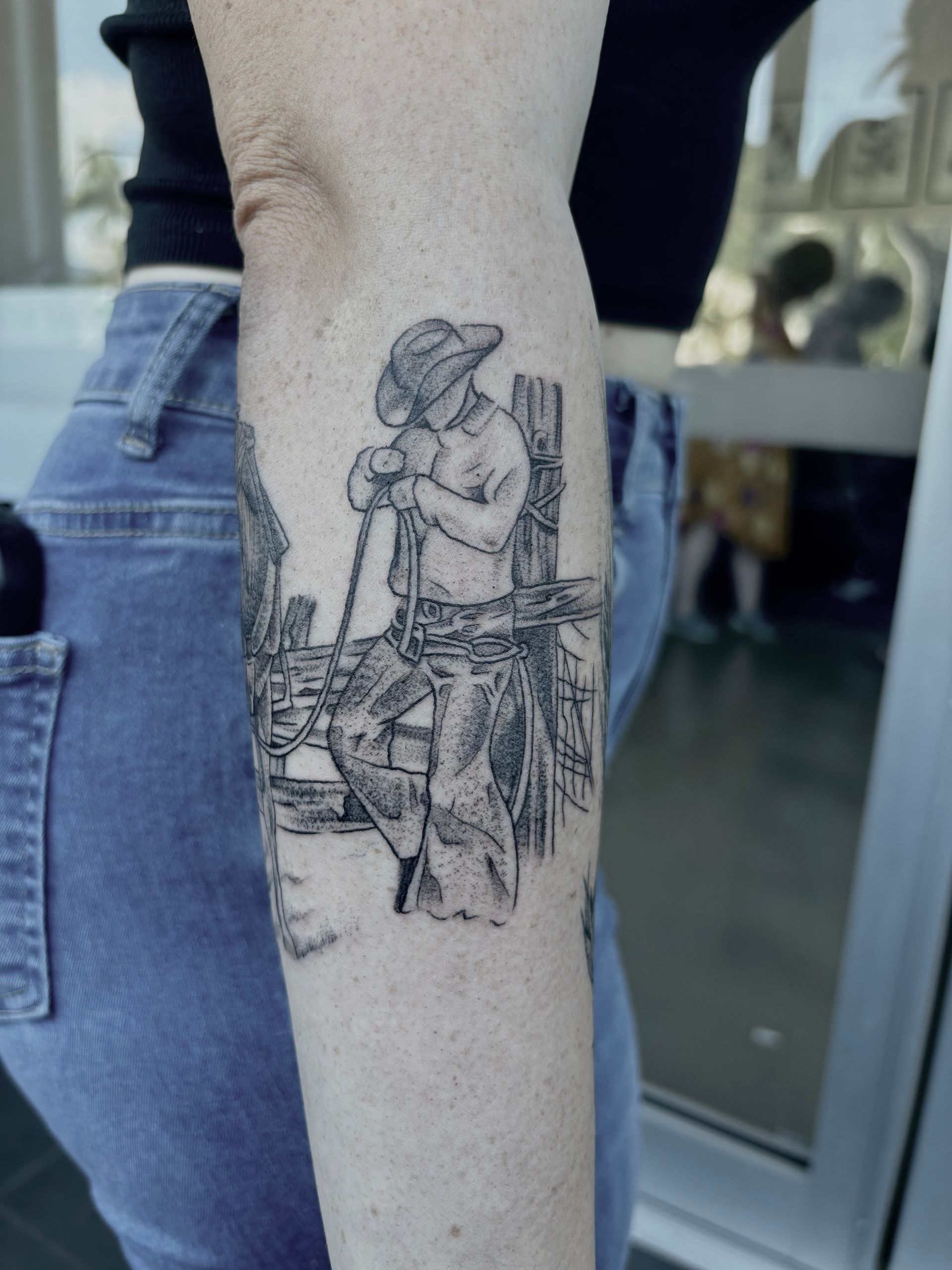Cowboy tattoo on arm, resting on a fence, in a black and white drawing style. — Pins and Needles Tattoo in Smithfield, QLD