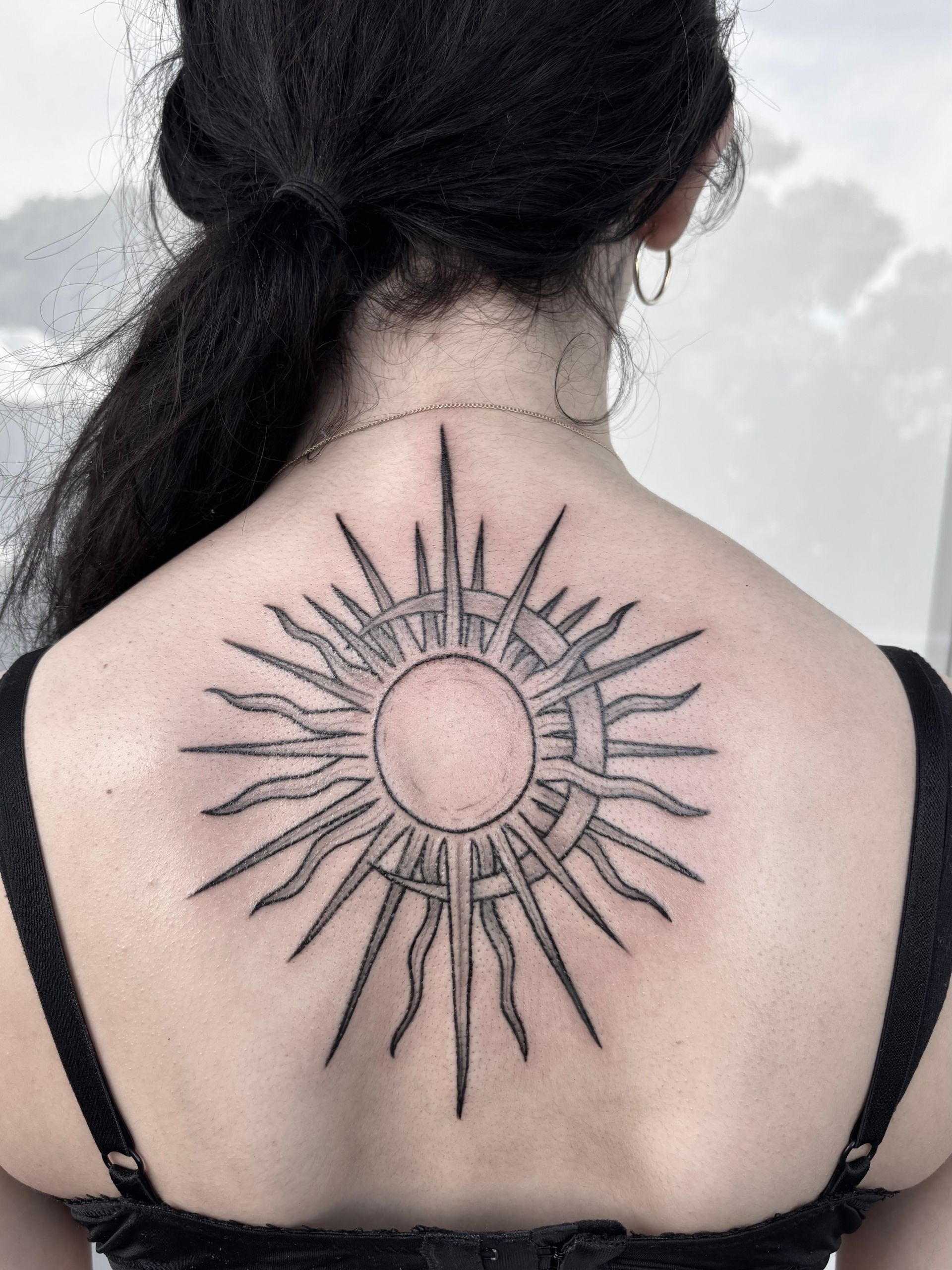 Woman with blonde hair, black tattoo on chest and shoulders, outdoors.