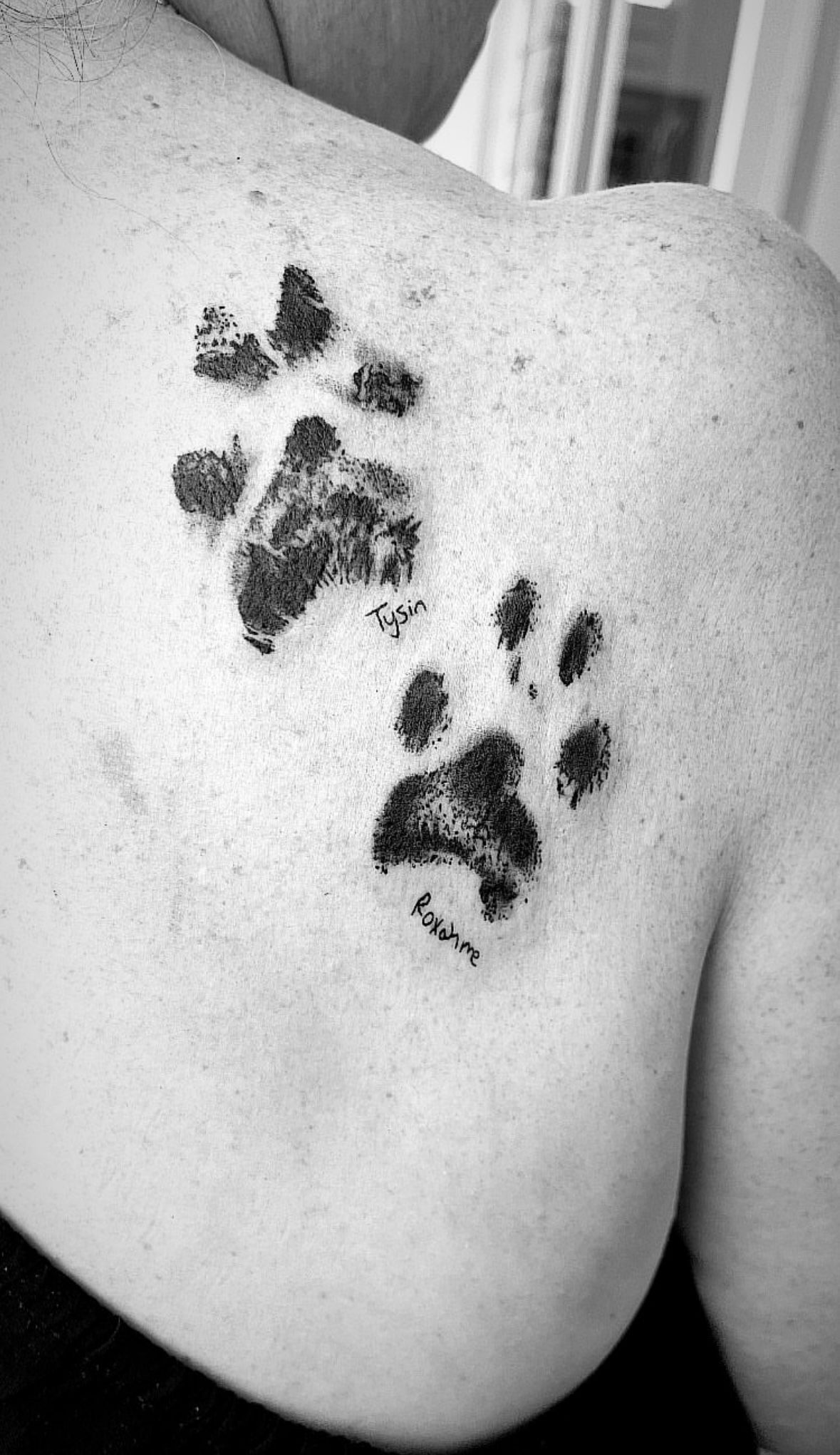 Black and white photo of two dog paw print tattoos on a shoulder. 