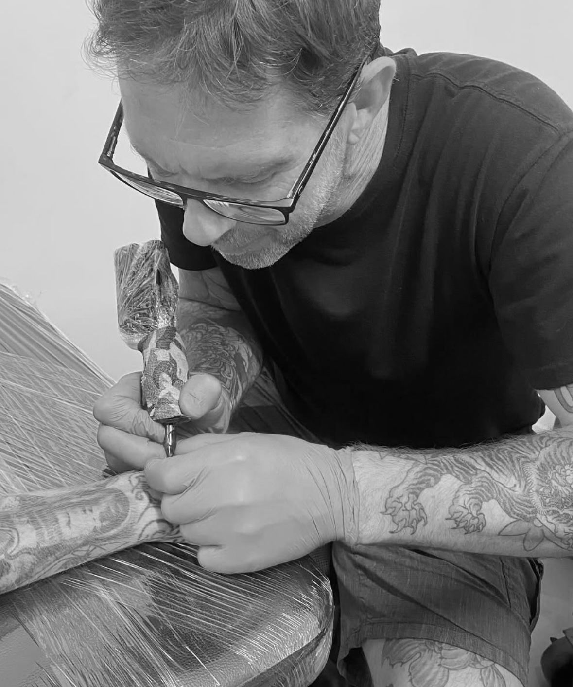 Tattoo Artist in Blue Gloves, Wearing Glasses, Tattooing a Forearm in Studio — Pins and Needles Tattoo in Trinity Beach, QLD
