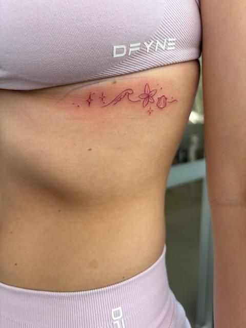 Pink ribcage tattoo: stars, wave, flower, on a person wearing a light pink sports bra. — Pins and Needles Tattoo in Smithfield, QLD