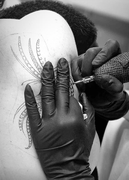 Person receiving a tattoo of an octopus design on their back. Black gloves hold tattoo gun. — Pins and Needles Tattoo in Smithfield, QLD