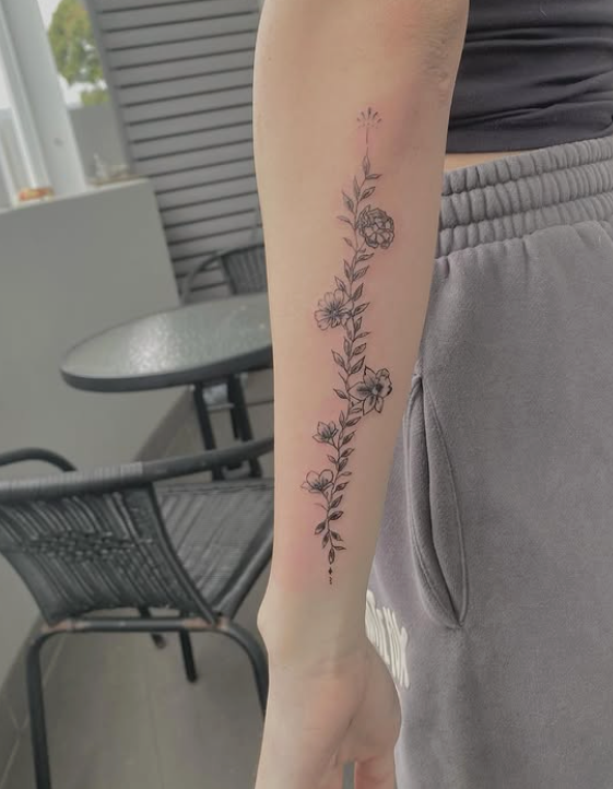 Arm with a delicate floral tattoo running vertically down the forearm, against a blurred outdoor background. — Pins and Needles Tattoo in Smithfield, QLD