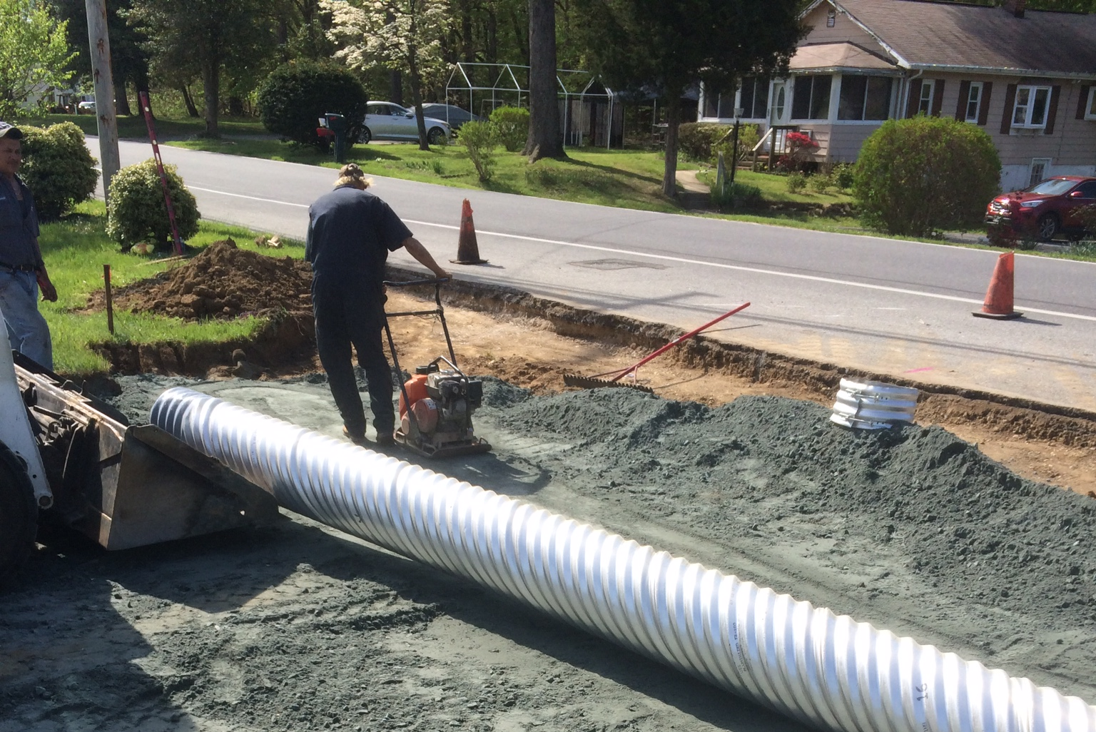 A man is standing next to a large pipe on the side of the road.