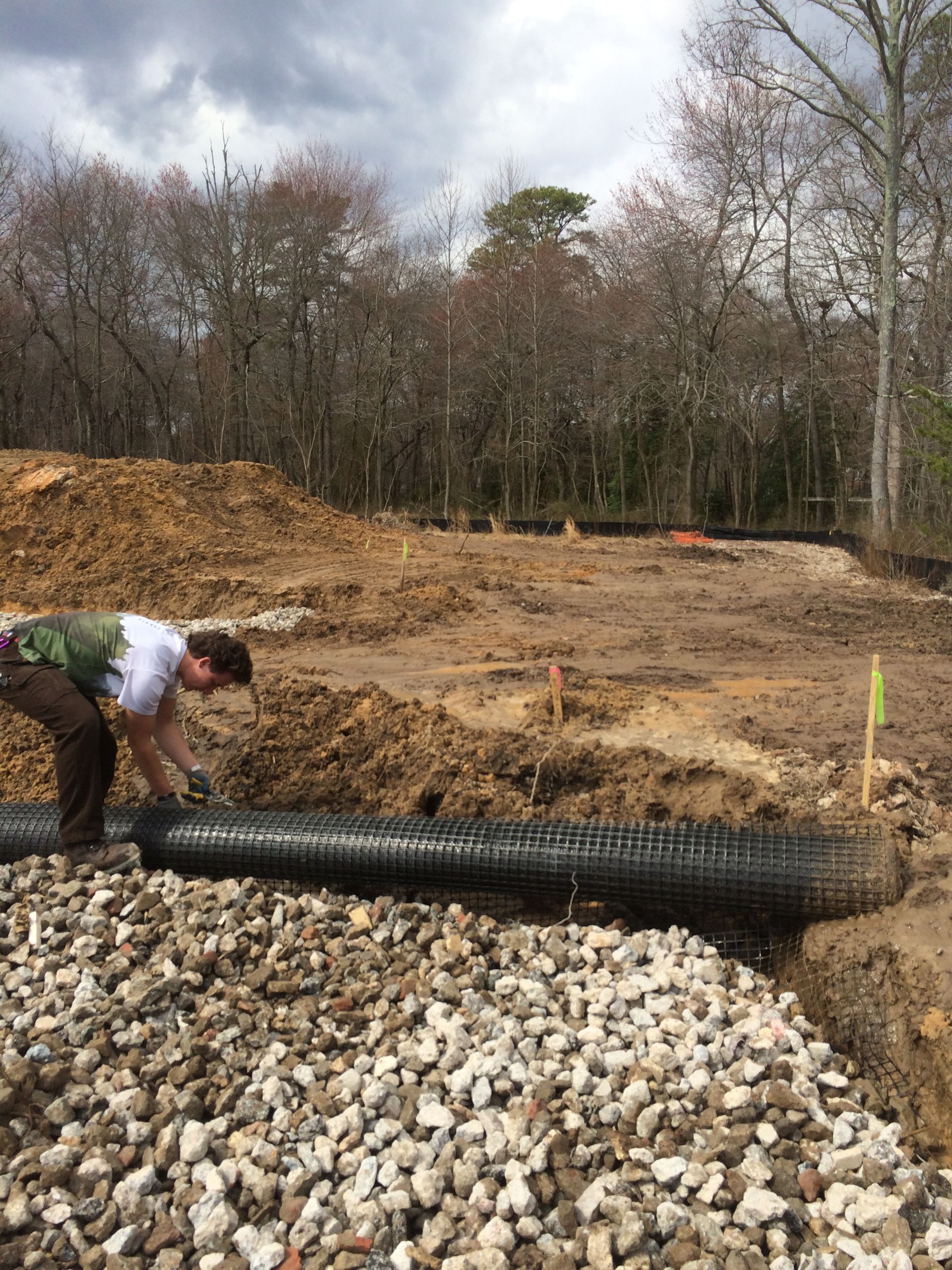 A man is working on a pipe in a pile of gravel.