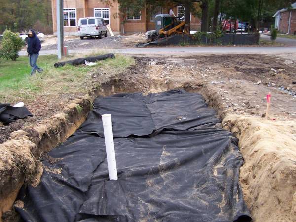 A white pipe is laying in the dirt next to a black tarp.